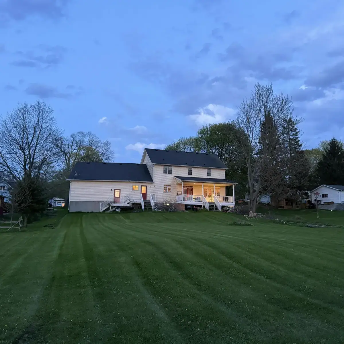 Striped backyard lawn at dusk behind a white farmhouse